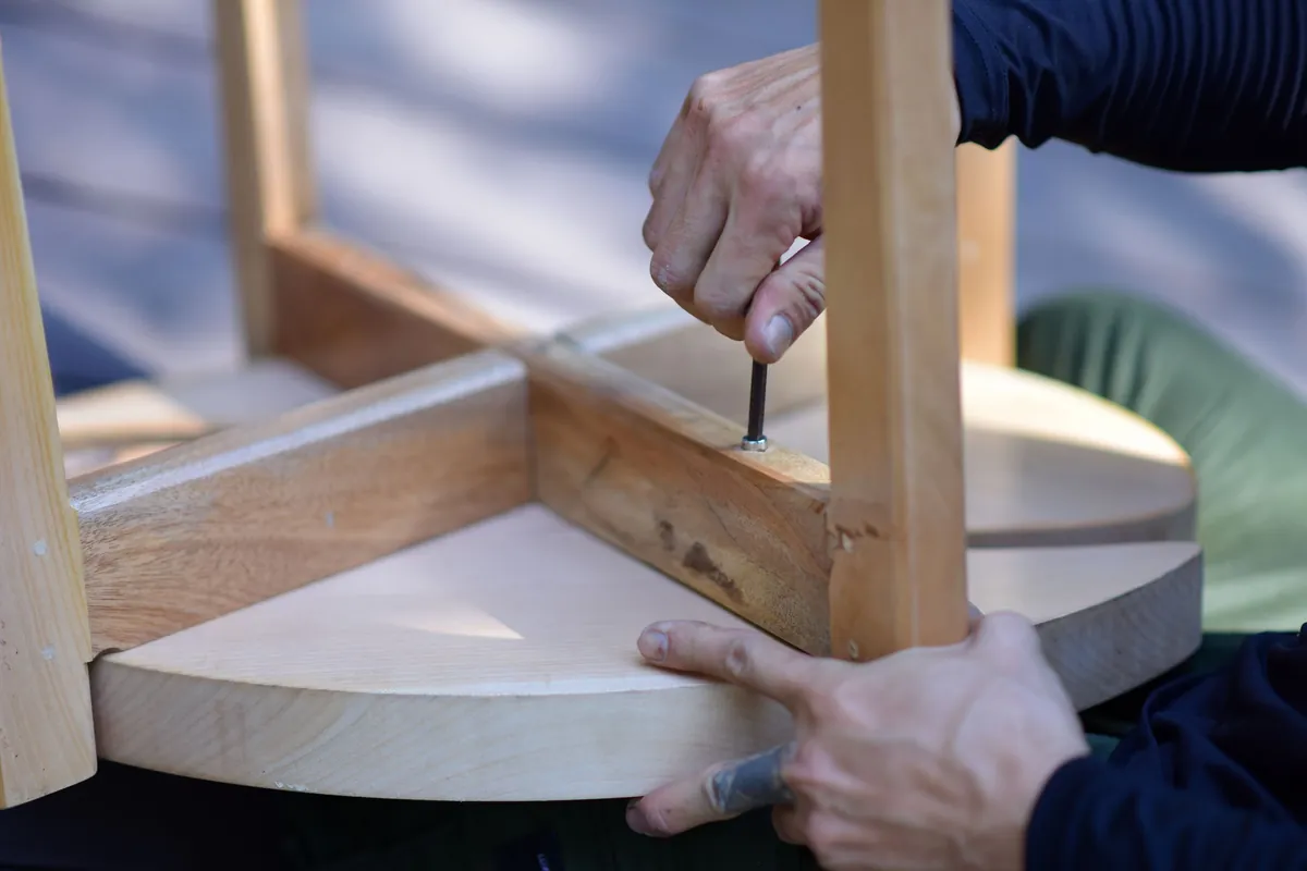 A handyman screwing the legs onto a solid-wood table during furniture assembly