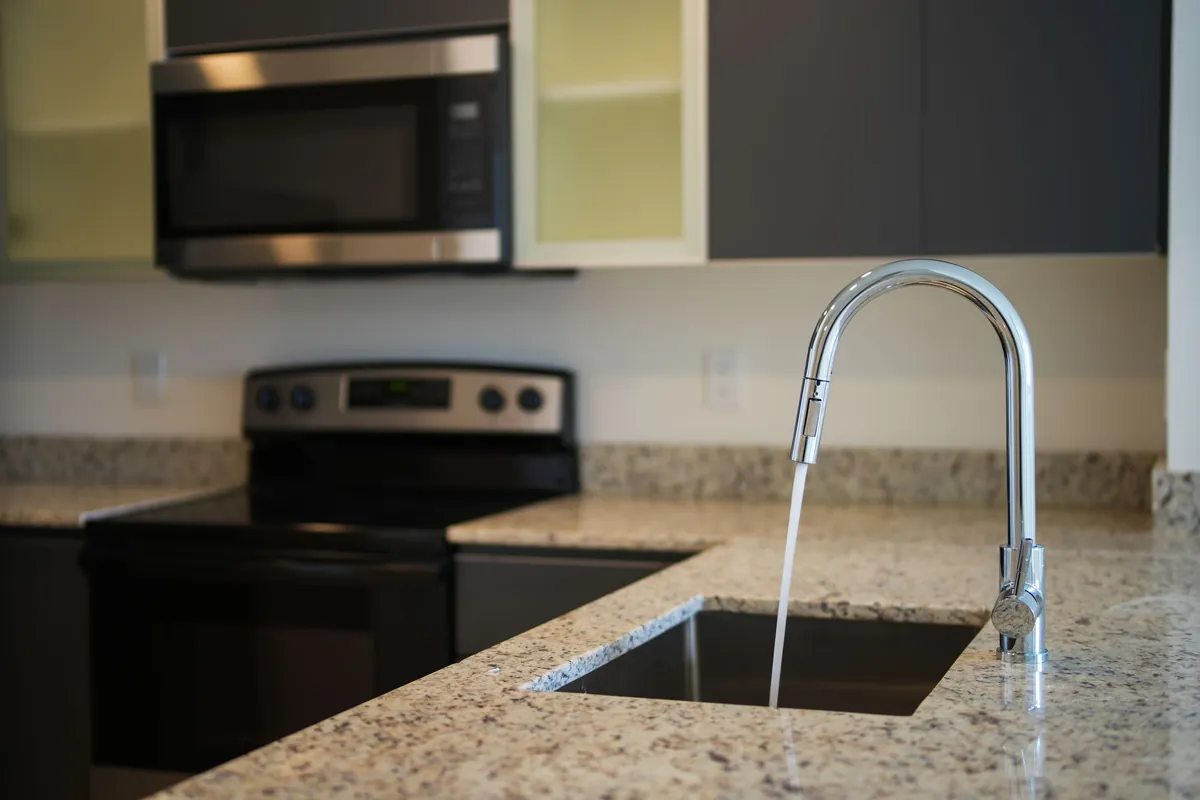 A new pull-down faucet running into an undermount sink in a granite kitchen counter