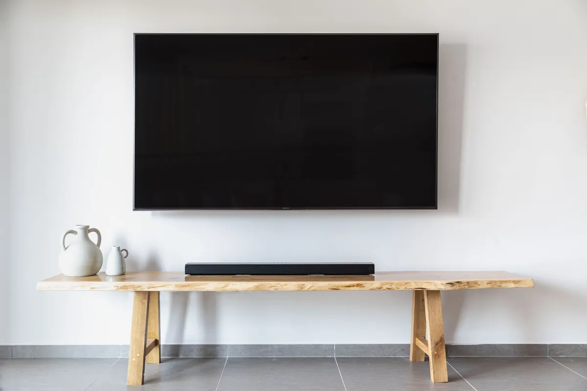 A large TV mounted level on a white living room wall with the wires hidden, above a wooden bench and soundbar